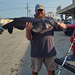 With a big smile on his face, Justin Hall poses outdoors by a fishing pole and pickup truck with his record-breaking channel catfish.