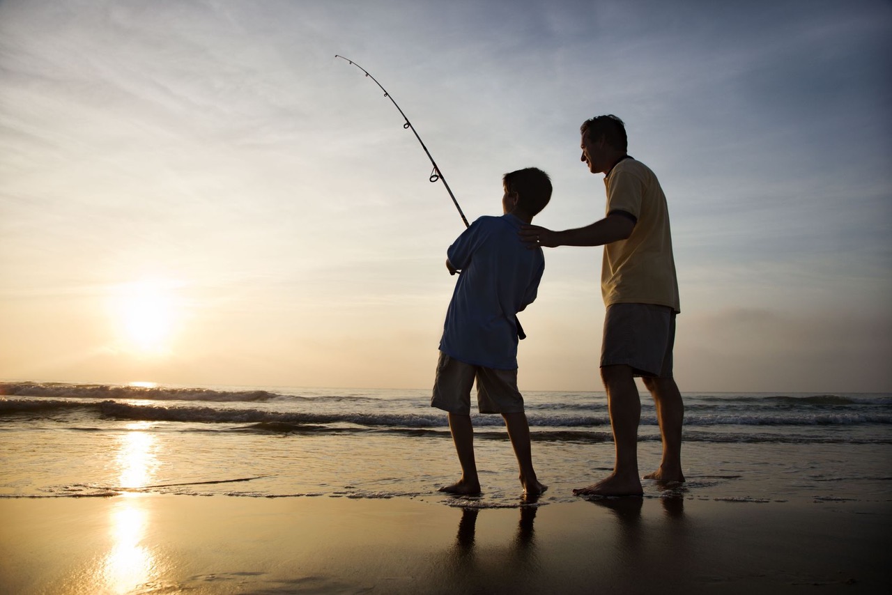 father and son fishing on the beach at sunset