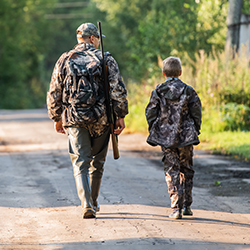 Hunting section link. Image depicts a father and son in camo walking away along a road.