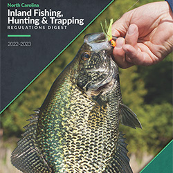 Inland Fishing, Hunting and Trapping Regulations Digest link. Image depicts the cover of the Digest where a hand is holding a fish they just caught.