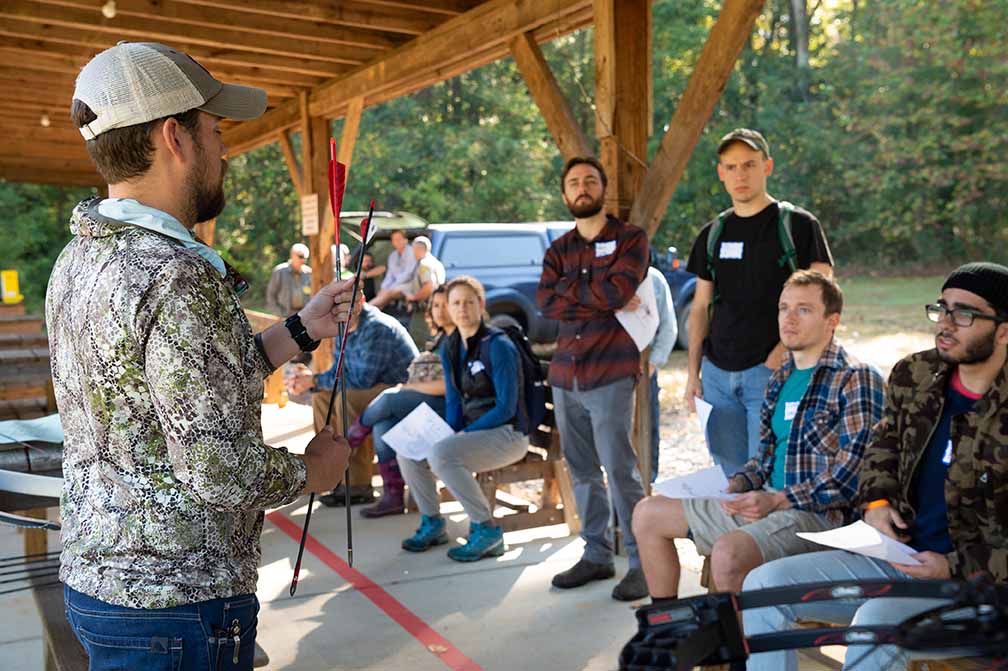 a Learn to Hunt program instructor holds two red-tipped arrows while teaching a class outdoors